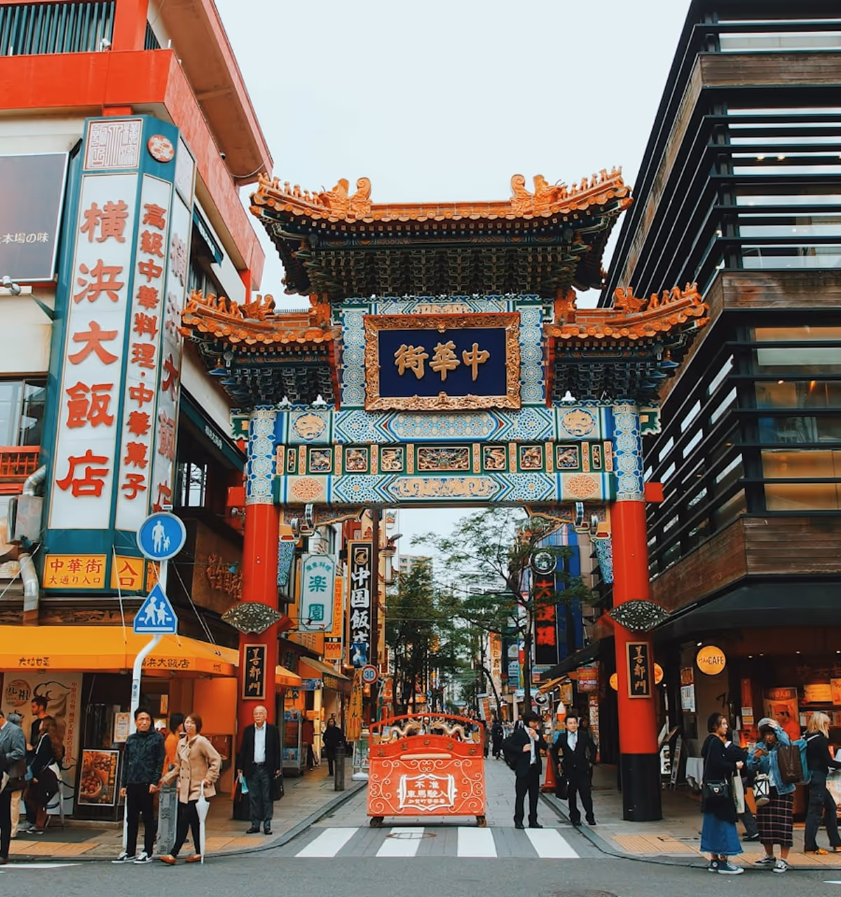 Traditional Chinese archway gate with ornate blue, red, and gold designs at the entrance to a busy street with pedestrians and shops.