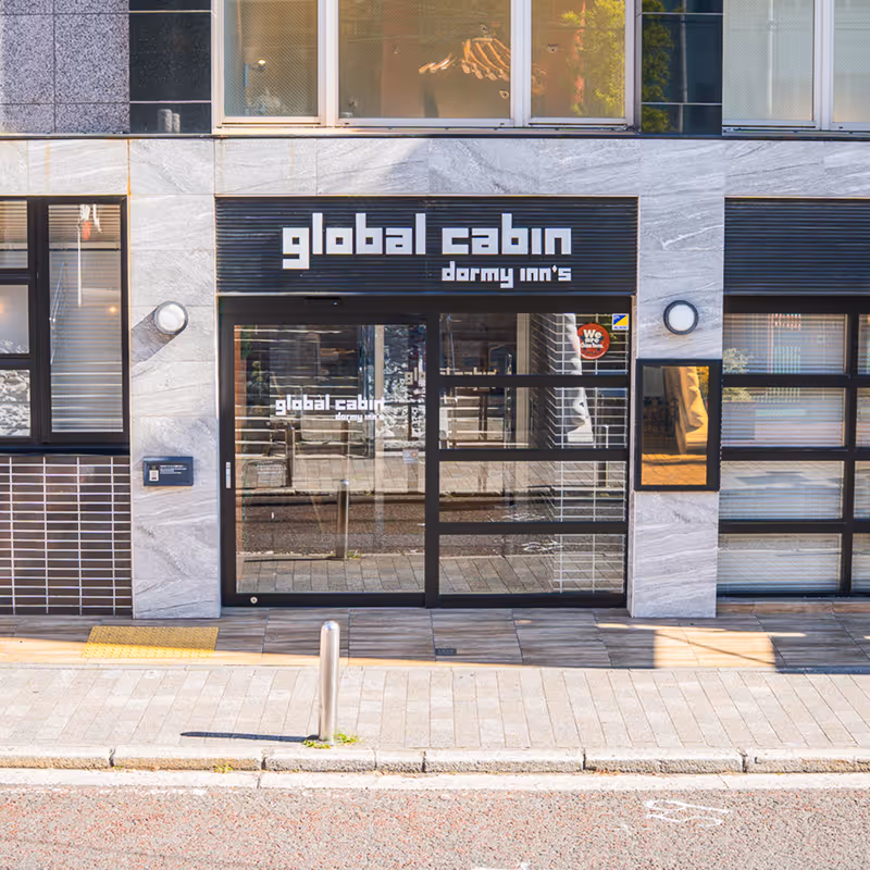 Entrance to global cabin (Dormy Inn) with glass doors and modern gray marble exterior.
