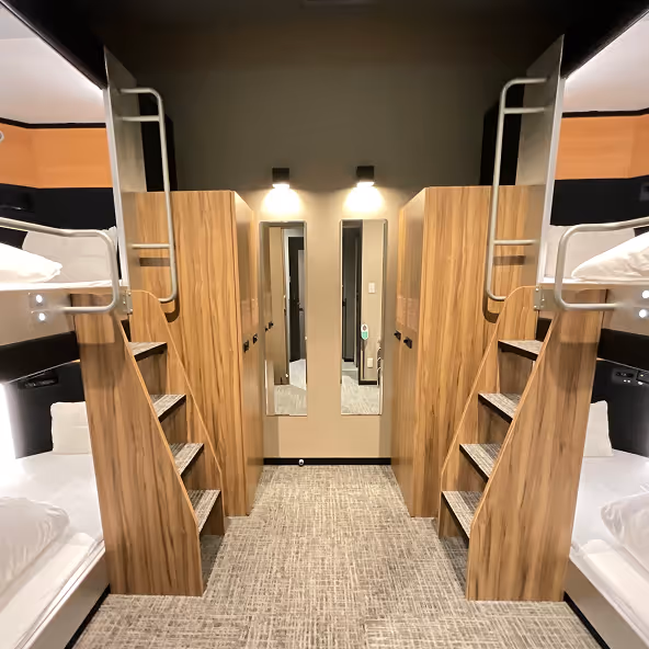 Modern dormitory room with wooden bunk beds, stairs, and two full-length mirrors on the far wall.