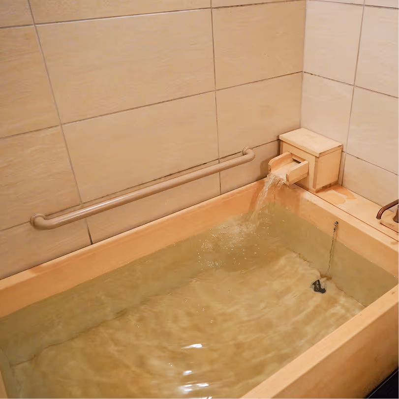 Water flowing into a beige tiled bathtub with a handrail on the wall.