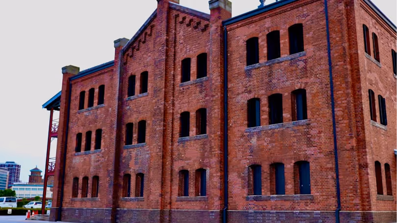 Large red brick warehouse building with multiple evenly spaced windows and a clear sky background.