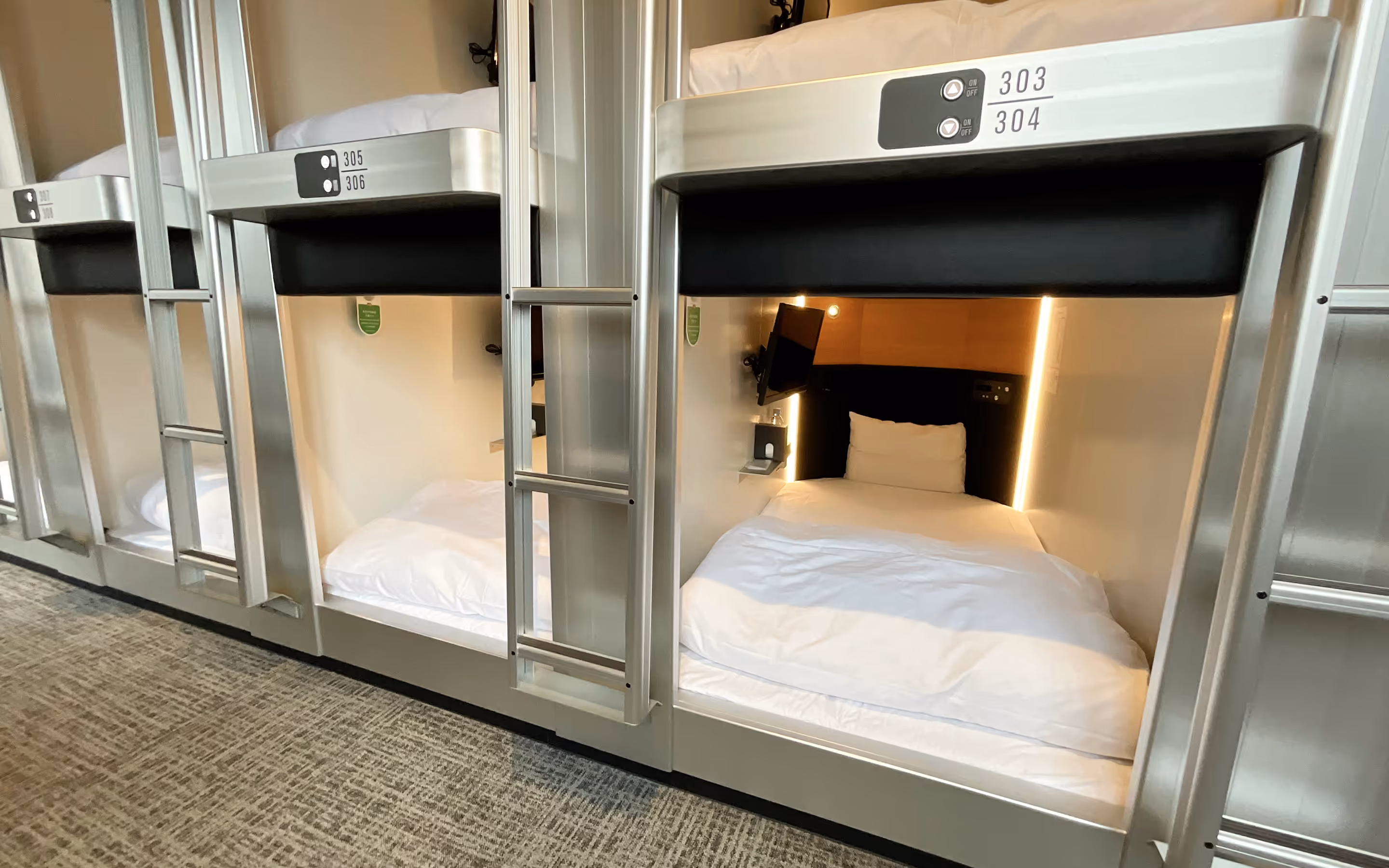 Modern pod-style sleeping units with white bedding, built-in lighting, and mounted TV screens.