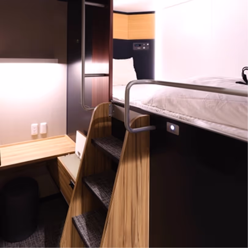 Compact modern bunk bed setup with wooden steps, built-in desk, and storage drawer in a small room.