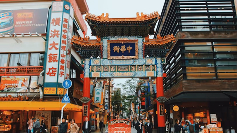 Ornate traditional gate marking the entrance to a busy street lined with shops and restaurants, with people walking around.