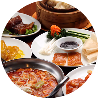 Assorted Chinese dishes including dim sum, braised pork, sliced roasted meat with sauce, and spicy soup in a round metal bowl.